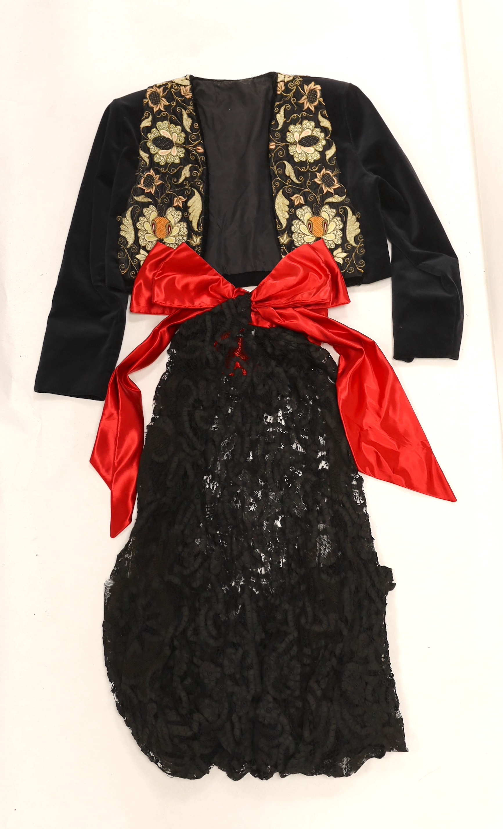 A velvet bolero with ornate polychrome silk embroidered and beaded panels, together with a full length black tape lace evening skirt (some damage) with red satin waisted sash